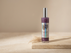 A bottle of Charlie Charlie Soap Co. Cinnamon Hearted Body Gel with a silver cap and a purple gel inside, displayed on a beige stone slab with dried grass against a warm beige background.