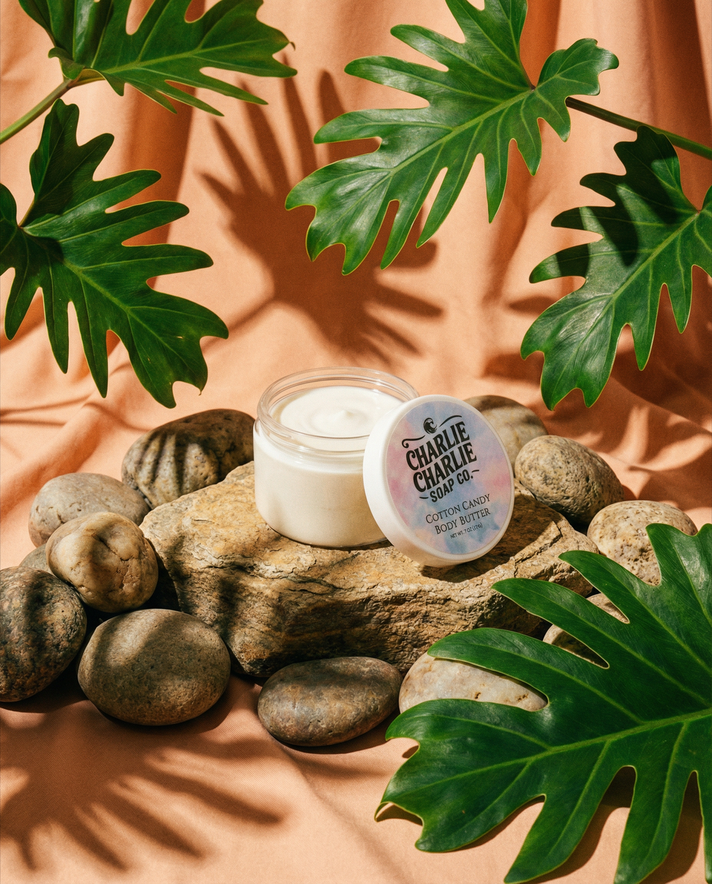 Jar of cream on rocks with green leaves and a peach-colored background