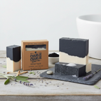 Two bars of black and white soap with a box labeled 'Charlie Soap Co.' on a wooden surface.