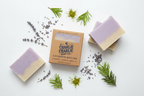 Two bars of lavender soap with a box labeled 'Charlie Charlie Soap Co.' on a white background with lavender and green leaves.
