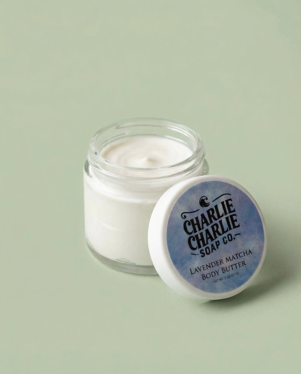 Jar of body butter with a blue label on a light green background