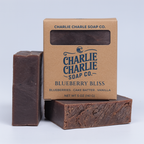 Two bars of soap and their packaging from Charlie Charlie Soap Co. on a light gray background