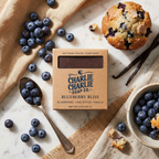 Charlie Charlie Soap Co. Blueberry Bliss soap bar with blueberries, a muffin, and vanilla beans on a marble surface.
