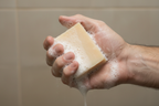 Hand holding a bar of soap with suds against a tiled wall background