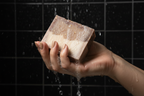 Hand holding a bar of soap under running water with a dark tiled background