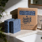 Two blue soap bars and their packaging on a bathroom counter.