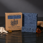 Blue soap bar with packaging labeled 'Charlie Charlie Soap Co. Deep Water Drift' on a dark surface.