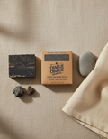 Bar of soap, packaging, and stones on a textured beige surface
