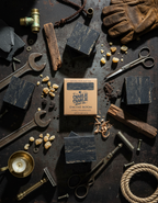 Bar of soap with packaging surrounded by tools and items on a dark surface