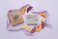 Bar of soap with packaging and fruit slices on a light purple background