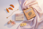 Perfume bottle, soap bar, and packaging on a light pink fabric background