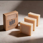 Three bars of soap and a box from Charlie Charlie Soap Co on a neutral background