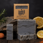 Bar of soap with packaging labeled 'Charlie Charlie Soap Co.' on a rustic background with lemons and rosemary.