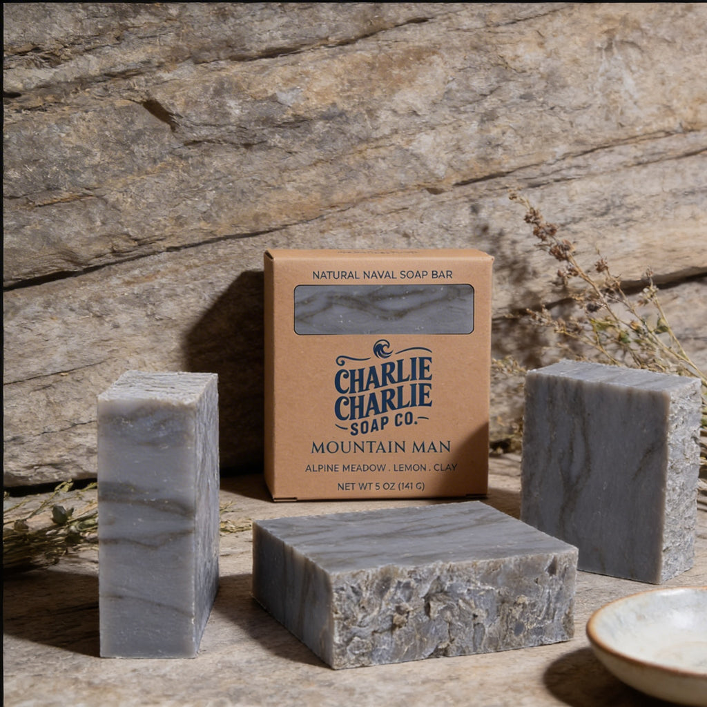 Three bars of soap and a box from Charlie Charlie Soap Co on a stone surface with a natural background.