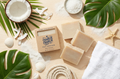 Bar of soap with packaging on a beach-themed surface with coconut, shells, and leaves.