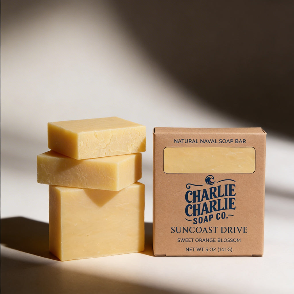 Three natural soap bars stacked next to a cardboard box labeled 'Charlie Charlie Soap Co.' on a neutral background.